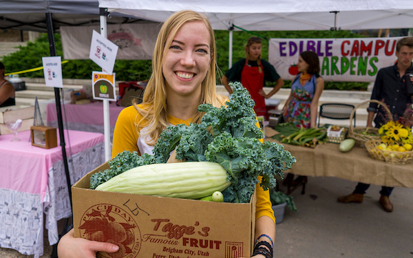 woman holding a box of produce at a farmers market